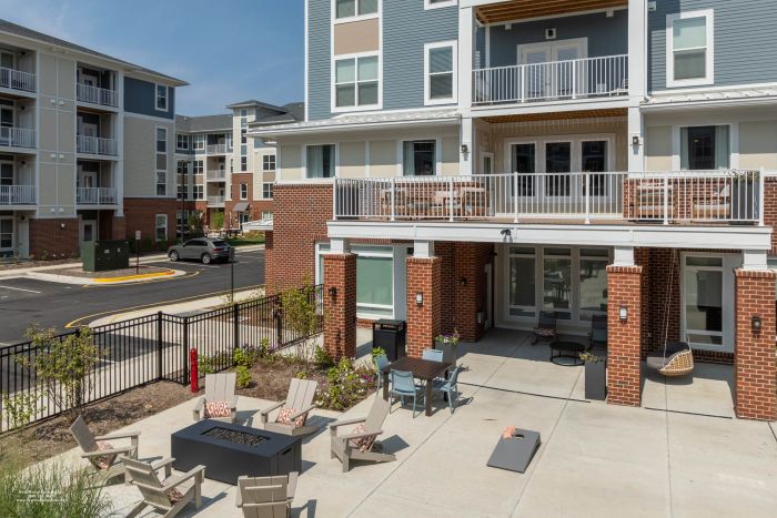 Attain at Towne Centre apartment homes with Apartment building patio with chairs around a fire pit, tables, and balconies above on a sunny day.