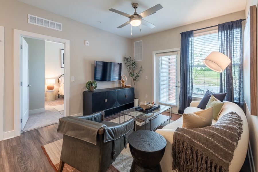 Attain at Towne Centre apartment homes with Modern living room with neutral tones, sofa, TV, glass coffee table, and large windows letting in natural light.