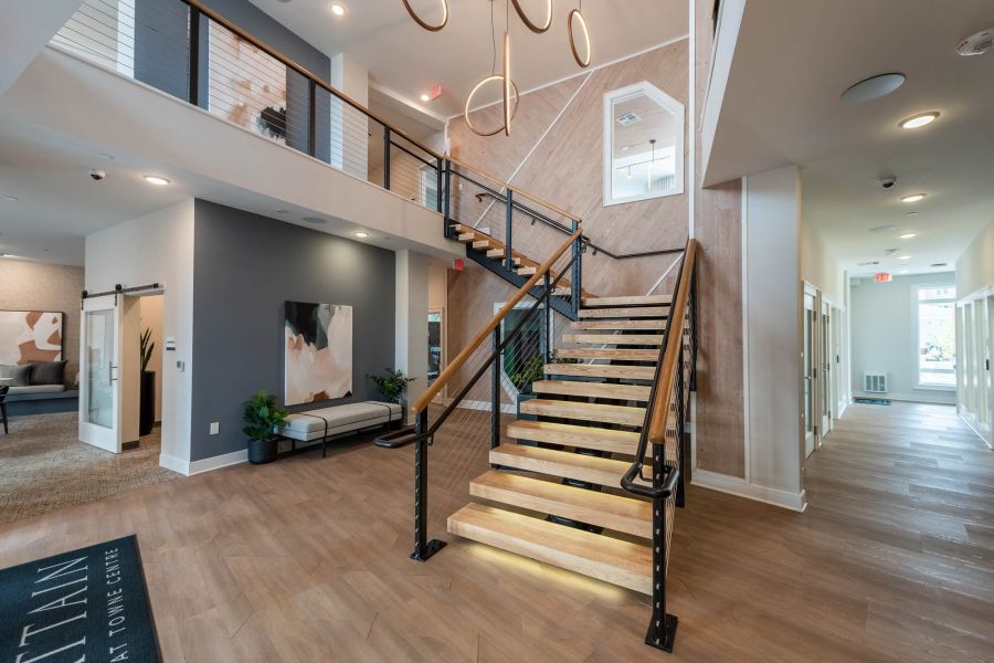 Attain at Towne Centre apartment homes with Modern lobby with wooden stairs, abstract chandelier, and seating area, featuring natural light and clean design.
