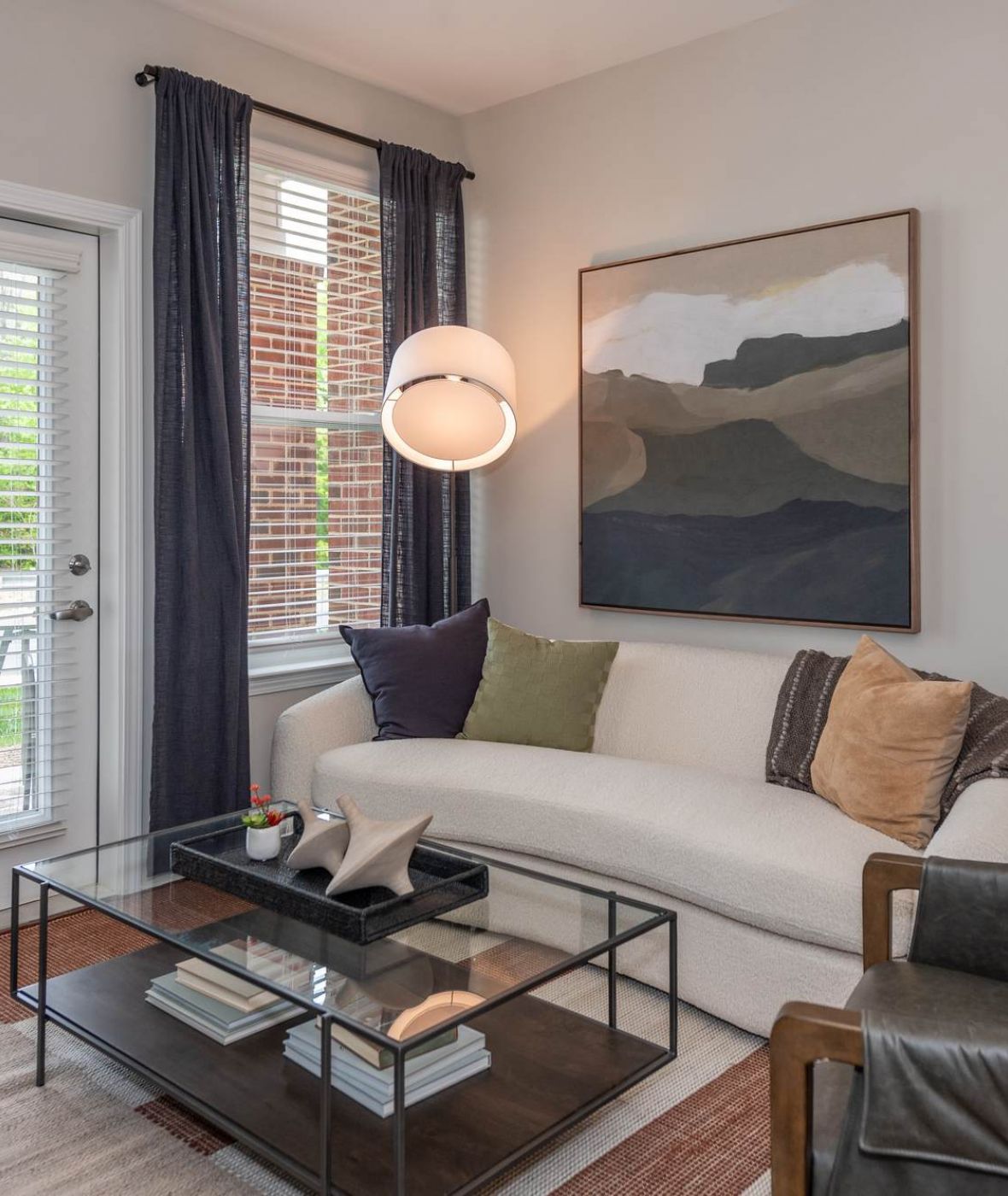 Attain at Towne Centre apartment homes with Modern living room with a white sofa, glass coffee table, abstract art, and a window with blinds and curtains.