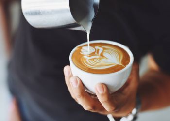 Attain at Towne Center apartment homes with Hand holding a cup of coffee with latte art as milk is being poured into it.