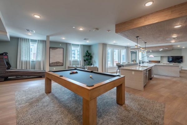 Attain at Towne Centre apartment homes with Modern game room with a pool table, treadmill, kitchen island, and lounge area with TV and windows.
