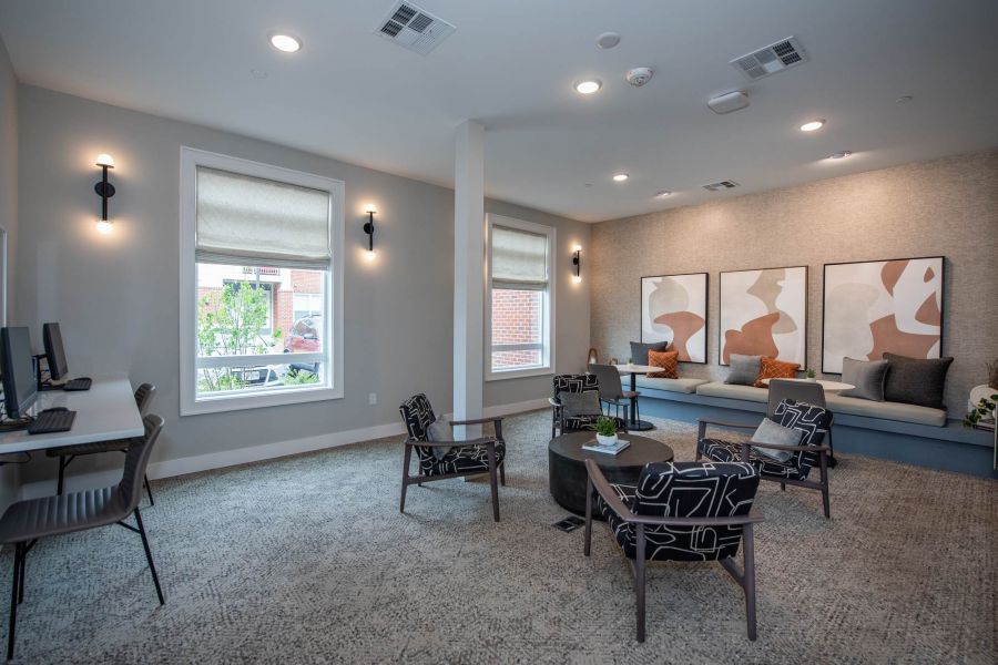 Attain at Towne Centre apartment homes with Modern lounge area with patterned chairs, wall art, computers, large windows, and neutral decor.
