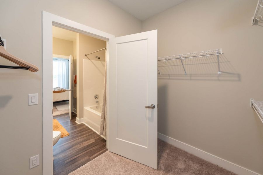 Attain at Towne Centre apartment homes with Empty walk-in closet with carpet, open door to a bathroom with a tub, shower curtain, and wood flooring.