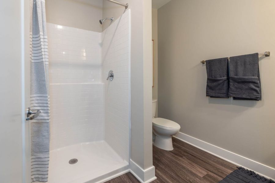 Attain at Towne Centre apartment homes with Modern bathroom with a white walk-in shower, striped curtain, toilet, and dark towels on a rack.