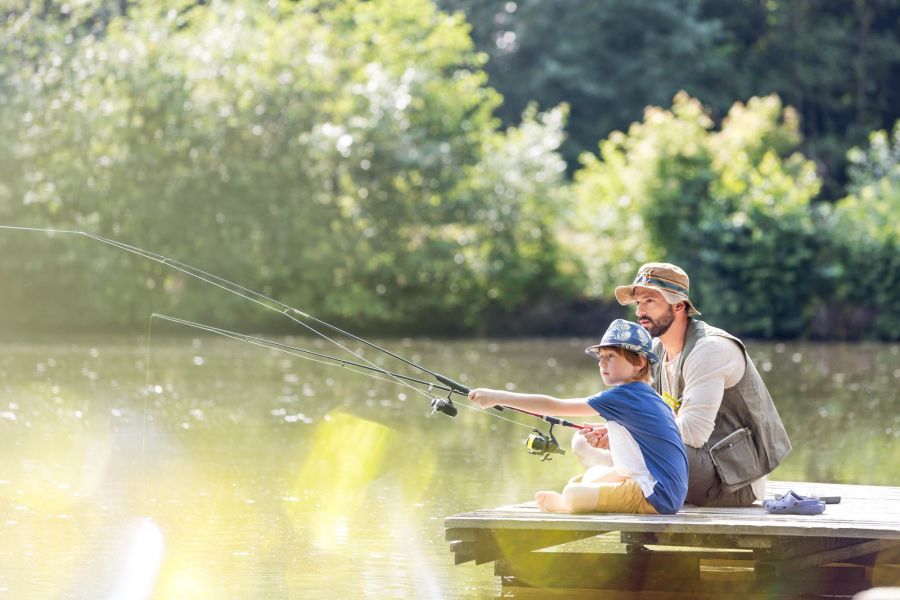 Attain at Towne Centre apartment homes with Man and child sitting on a wooden dock, fishing together by a calm lake on a sunny day.