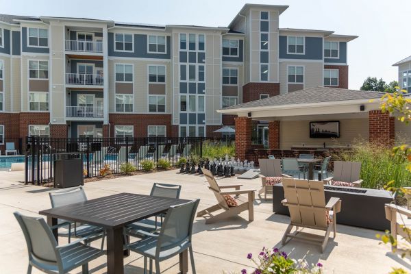 Attain at Towne Centre apartment homes with Outdoor lounge area with tables, chairs, giant chess set, and pool in front of a modern apartment building.