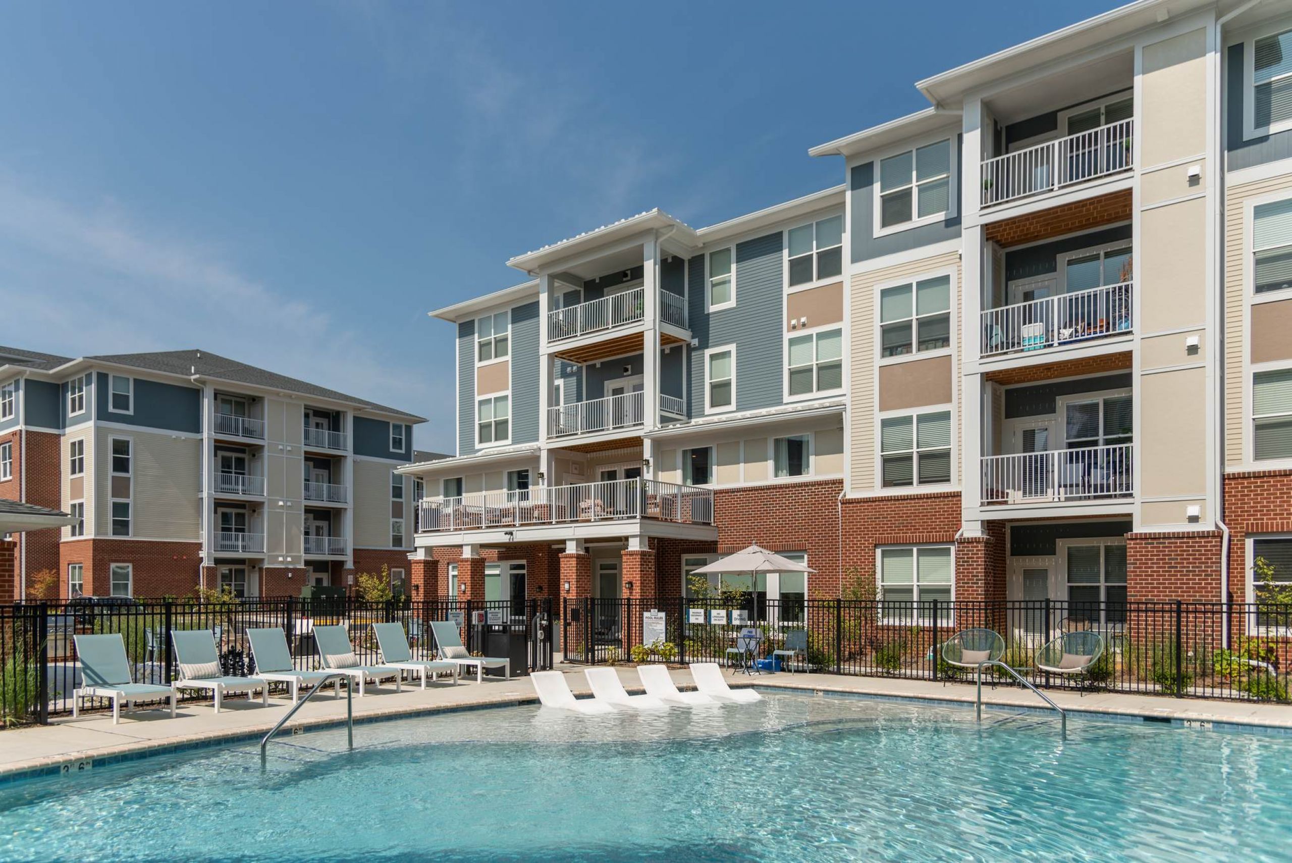 Attain at Towne Centre apartment homes with Outdoor swimming pool with lounge chairs in front of modern apartment buildings on a sunny day.