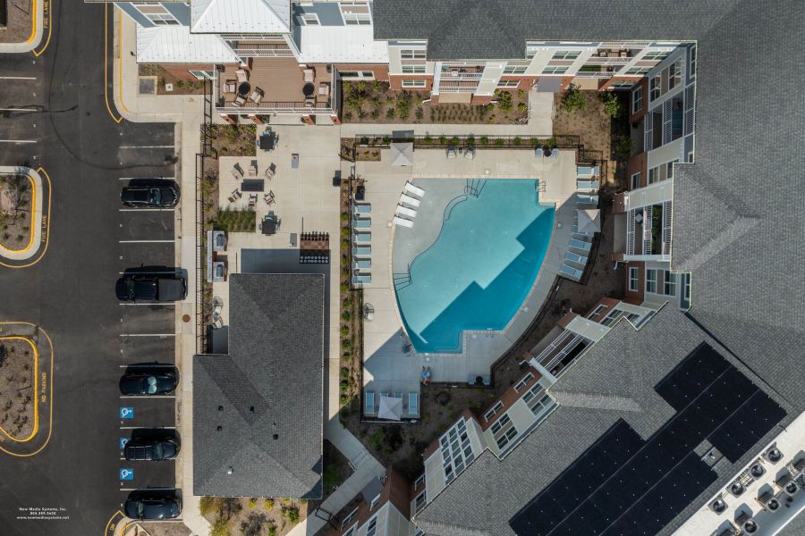 Attain at Towne Centre apartment homes with Aerial view of an outdoor swimming pool surrounded by lounge chairs and buildings, with nearby parked cars.
