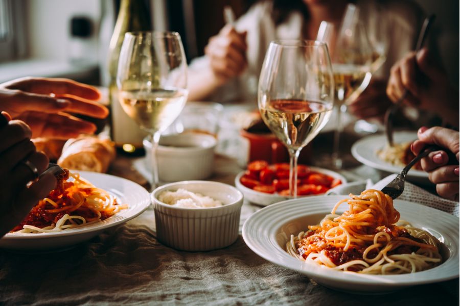 Attain on 5th apartment homes with Four people enjoy spaghetti and white wine at a cozy, sunlit dining table set with small dishes and glasses.
