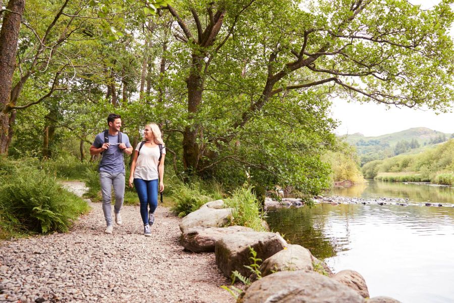 Attain at Towne Centre apartment homes with A couple walks along a tree-lined lakeside trail, carrying backpacks on a bright, clear day.